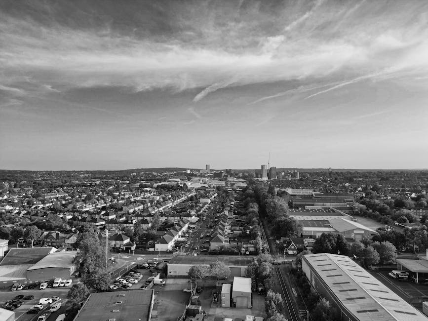 A black and white aerial photograph showing a large industrial and commercial area near a river with numerous storage tanks, warehouses, and crane equipment visible in the distance. In the foreground,